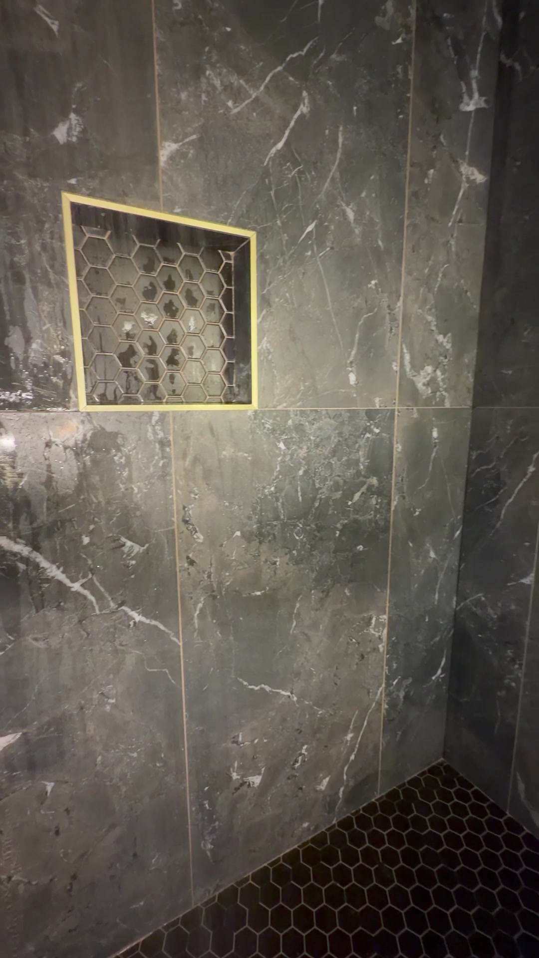 Black marble tile shower with brushed gold fixtures and honeycomb mosaic niche